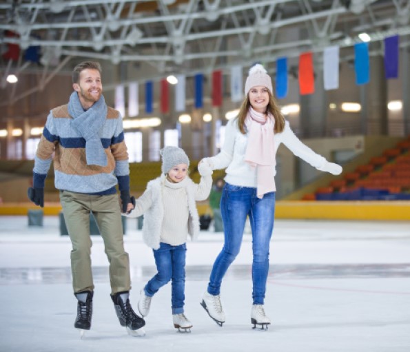 child holding hands and skating inbetween a woman and man at an indoor ice rink